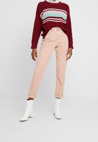 Pull bordeaux tricoté avec des rayures bleu clair, rose et blanches, associé à un jean taille haute rose clair et des bottines blanches.