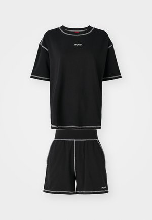 T-shirt nera in cotone a maniche corte con cuciture grigie e logo "HUGO" sul petto, abbinata a pantaloni corti neri con tasche laterali.