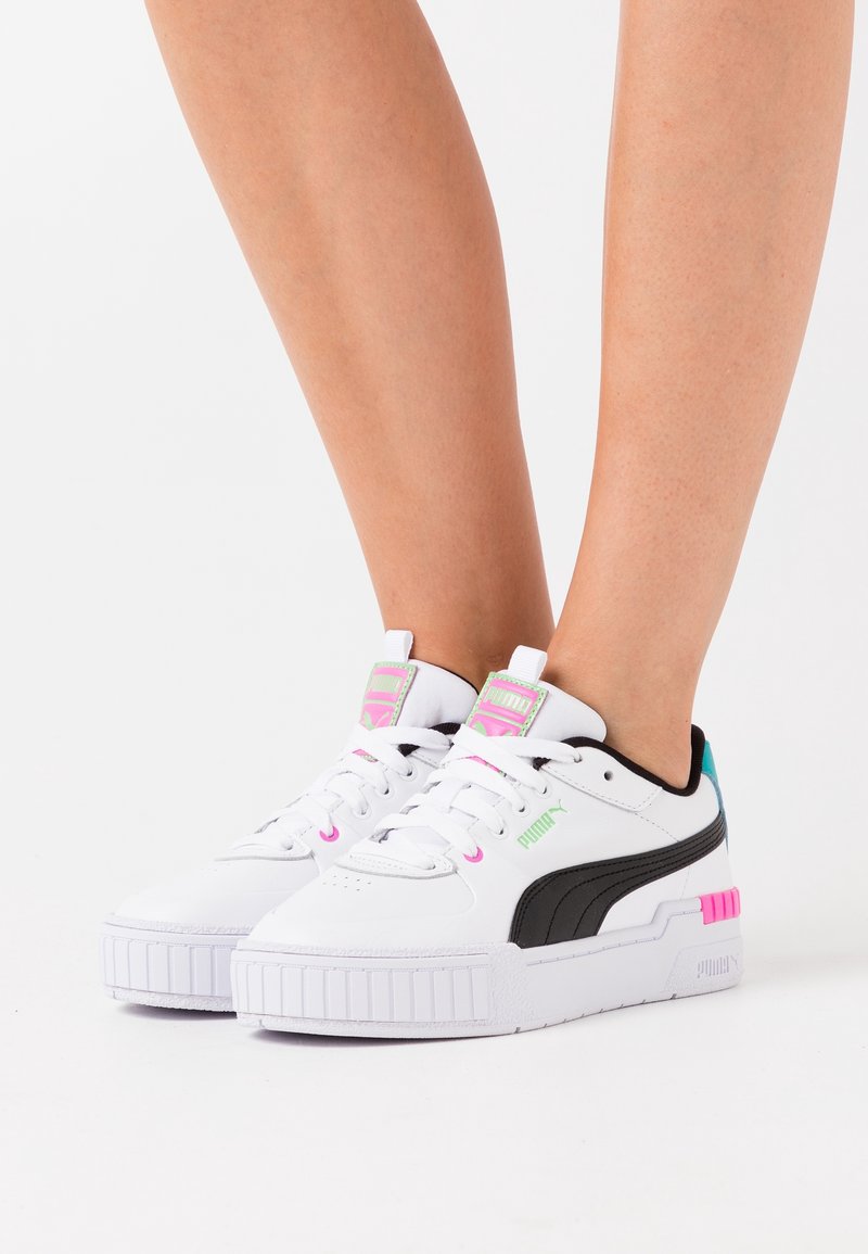 Baskets en cuir blanc avec des accents noirs et des détails colorés. Présentent une semelle texturée et un logo bien en vue sur la languette.