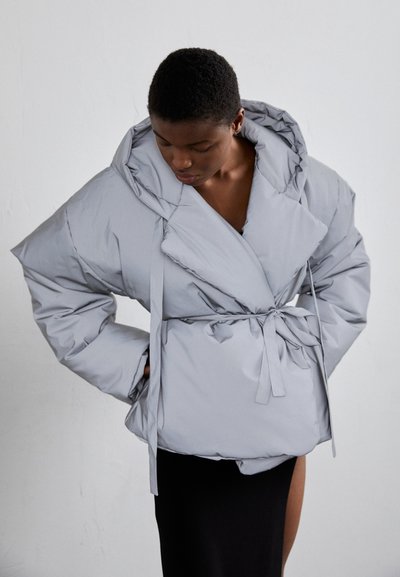 Giacca puffer grigia chiara con design avvolgente, colletto ampio e lacci in vita. Il materiale è liscio e imbottito, creando una texture morbida.