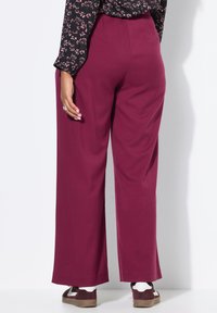 Brede broekspijpen in bordeauxrode stof. Gladde textuur met een hoge taille. Gepaard met casual schoenen met een bruin-wit ontwerp.
