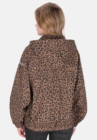 Ruskean leopardikuvioinen hupullinen takki, jossa väljä istuvuus, joustavat hihansuut ja kiristysnyörit helman kohdalla. Materiaali näyttää sileältä ja mattapintaiselta.