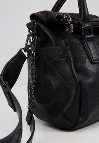 Sac à main en cuir noir avec motifs floraux embossés, fermeture éclair métallique, détail de chaîne en métal et bandoulière réglable avec fermoirs métalliques.