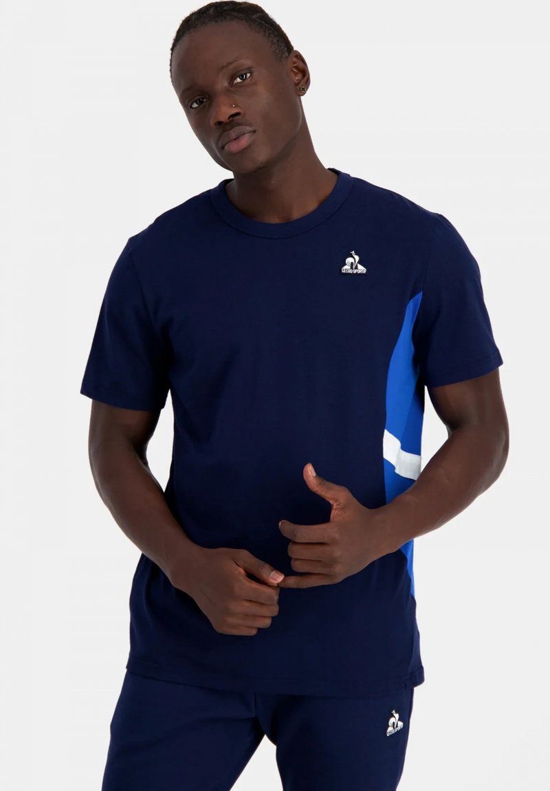Camiseta de manga corta azul marino con un diseño geométrico azul y blanco en el lateral; hecha de algodón; cuenta con un logo en el pecho.