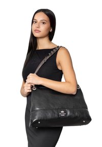 Sac à main en cuir noir avec une forme structurée, détail de poignet en chaîne argentée et accent de logo. Il présente une texture lisse et des clous en métal.