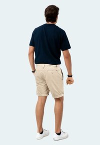 Navy crew-neck t-shirt and beige shorts with rolled cuffs. Shorts feature back pockets and a smooth cotton texture. White sneakers complete the outfit.