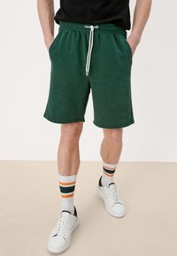 Shorts verts en mélange de coton avec taille élastique et cordon de serrage ajustable. Dotés de poches latérales et d'un détail logo sur la jambe gauche.