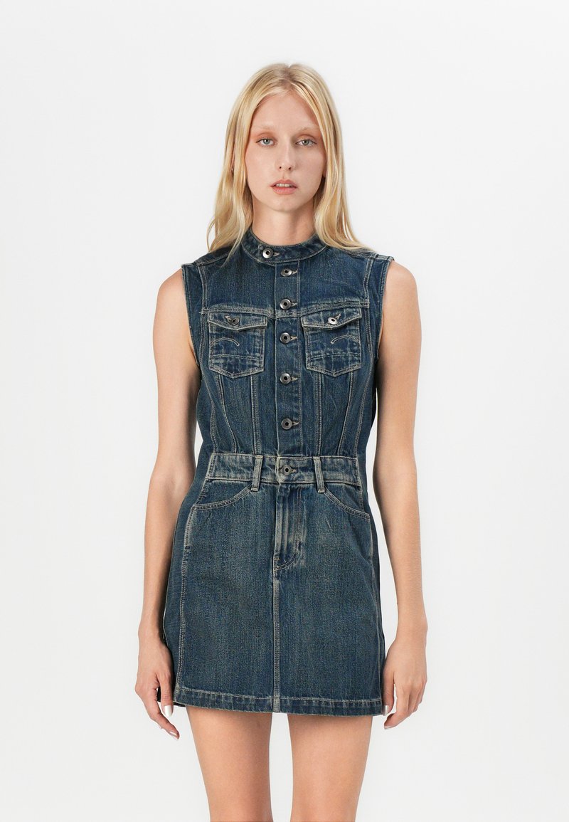 Denim dress with a fitted bodice, sleeveless design, and four front pockets. Dark blue wash with a belted waist and button closure.