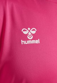 Roze sportshirt met een gladde textuur en een wit "hummel" logo met een geometrisch bijontwerp aan de linkerkant.