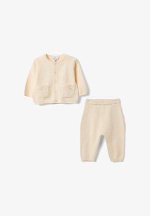 Weiche, cremefarbene Babystrickjacke mit Knöpfen und passenden Strickhosen mit elastischem Bund vor weißem Hintergrund.