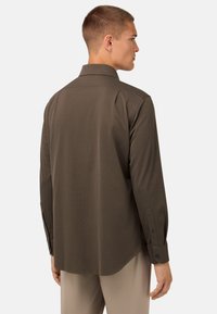 Olīvu zaļa krekls ar garām piedurknēm, izgatavots no gludas auduma. Tam ir klasiskā apkakle, pogājami aproces un izliekts apakšmalas dizains.