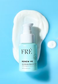 Jasnoniebieska butelka serum przeciwzmarszczkowego FRÉ Renew Me z bakuchiolem, z białą pompką, otoczona białym kremem na niebieskim tle.