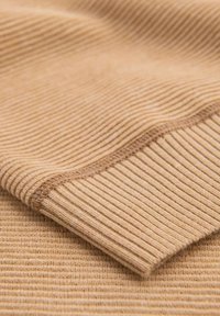 Tessuto beige a coste con una superficie testurizzata, caratterizzato da sottili strisce verticali e un orlo liscio. Lo spessore varia, conferendo un aspetto morbido.