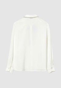 Blusa bianca a maniche lunghe con dettagli in perle lungo il colletto e bottoni in perla sui polsini, vista da dietro.