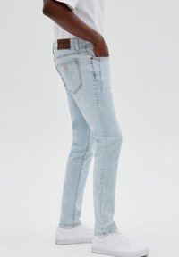 Ljusblå denimjeans med slim fit, fem fickor och en brun logopatch på baksidan av midjan. Matchas med vita sneakers.