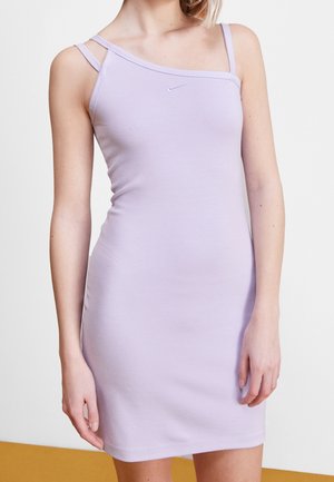 Femme portant une robe sans manches ajustée lilas avec des doubles bretelles fines et un petit logo Nike sur la poitrine, se tenant devant un fond uni.