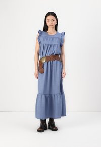 Blå chambray-kjole med volangermer, lagdelt kant og et brunt lærbelte med sirkulære detaljer og et dekorativt spenne. Svarte ankelstøvel.