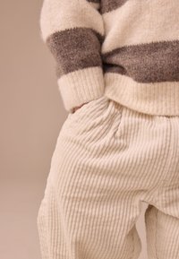 Pull en maille rayé crème et brun, associé à un pantalon côtelé texturé beige clair. Coupe décontractée avec poches latérales.