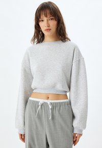 Sudadera gris corta con mangas largas, puños acanalados y un acabado texturizado, combinada con pantalones grises de rayas con cintura ajustable.