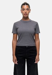 T-shirt grigio, tagliato con maniche corte e colletto rotondo a costine, abbinato a pantaloni neri a gamba larga con tasche anteriori e dettagli in metallo.