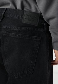 Zwarte denim jeans met een vierkante achterzak en een zwart leren merketiket, met een gestructureerde afwerking en subtiele stikdetails.