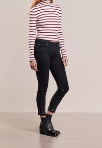 Svarta jeans med pärlbroderier i fållen, kombinerat med en randig turtleneck i rött och vitt. Slätt tyg, åtsittande design.