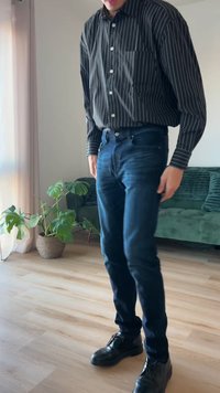 Σκούρα μπλε τζιν με στενή εφαρμογή, σε συνδυασμό με μια μαύρη και λευκή ριγέ μπλούζα. Μαύρα δερμάτινα παπούτσια. Εσωτερικός χώρος με πράσινο καναπέ και φυτά.