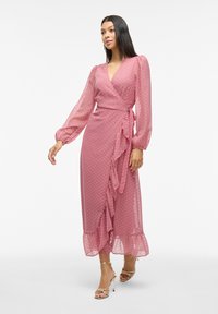 Abito lungo rosa avvolgente realizzato in tessuto trasparente con pois, caratterizzato da maniche a sbuffo, orlo arricciato e dettaglio con cintura da annodare in vita.