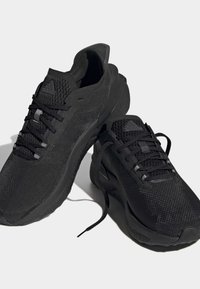 Černé sportovní boty s prodyšným síťovaným svrchním materiálem, texturovaným povrchem, plochými tkaničkami a polstrovanou podrážkou. Logo je výrazně umístěno na jazyku a boku boty.