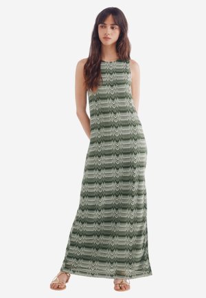 Maxi dress in green, featuring a textured zigzag pattern. Sleeveless design, made from lightweight fabric, paired with gold sandals.