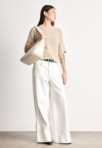 Šviesiai smėlio spalvos megztinis trumpomis rankovėmis, plačios baltos kelnės ir kreminės spalvos rankinė. Aprangą papildo juodas diržas ir juodi batai.