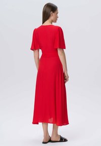 Rotes, knielanges Kleid mit kurzen, ausgestellten Ärmeln und tailliertem Schnitt. Hergestellt aus leichtem Stoff mit subtiler Textur und Rückenreißverschluss.