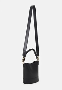 Czarna skórzana torebka typu bucket z skręcanym górnym uchwytem i długim regulowanym paskiem na ramię, przedstawiona wisząca na białym tle.