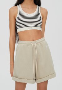 Soutien-gorge de sport cropped à rayures noir et blanc avec une étiquette à l'avant ; shorts beiges clairs à cordon de serrage avec ourlets retroussés et détail de logo.
