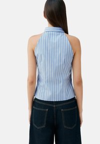 Top à col halter rayé bleu et blanc avec un dos ajusté et un ourlet légèrement arrondi. Le matériau semble lisse avec une texture légère.