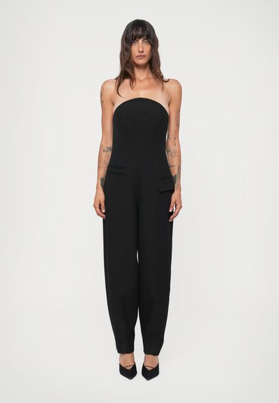 Zwarte strapless jumpsuit met een fitted lijfje, brede pijpen, twee voorkanten zakken en een gladde textuur. Voltooid met zwarte hakken.
