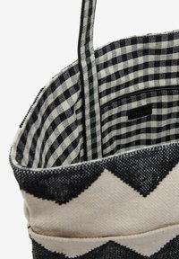Canvas tote bag with a black and white zigzag pattern, featuring a checked interior lining and a zippered pocket for storage.