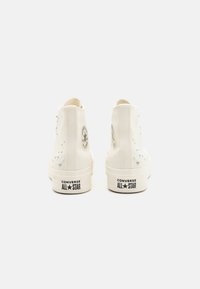 Λευκά ψηλά αθλητικά παπούτσια κατασκευασμένα από καμβά, με στρογγυλή μύτη, διακοσμητικές τρουκς στο εξωτερικό πλάι και το λογότυπο "Converse All Star" στην φτέρνα.