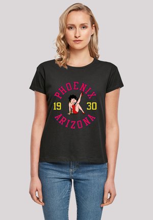 Eine Frau trägt ein schwarzes T-Shirt mit einem roten, gelben und blauen Betty Boop-Graphic und dem Text "Phoenix Arizona 1930" und schaut nach vorne.