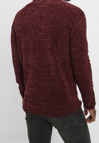 Bordowy sweter z teksturowanym splotem, okrągłym dekoltem i długimi rękawami. Charakteryzuje się luźnym krojem i subtelnym melanżowym wzorem.