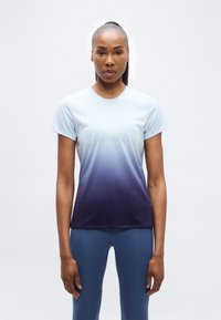 Γυναίκα που στέκεται και κοιτάζει μπροστά, φορώντας ένα κοντομάνικο t-shirt με ombre απόχρωση που ξεθωριάζει από ανοιχτό μπλε σε σκούρο μωβ και μπλε κολάν.