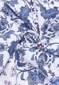 Bloemige stof met een witte achtergrond en complexe blauwe en bordeaux patronen, waarop bladeren en bloemen in een gestructureerde weving zijn afgebeeld.