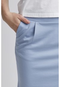 Ljusblå kjol i en slät tygkvalitet, med sidofickor och subtila veck vid midjan, ihopparad med en vit topp.