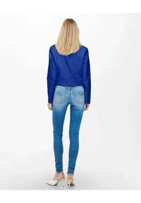 Skuren blå läderjacka över ljusblå skinny jeans; vita högklackade skor; slät textur och elegant design.