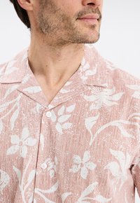 Camisa de manga corta tipo botón en color coral claro con estampado floral blanco, con cuello tipo camp y tejido texturizado. Dos botones visibles.