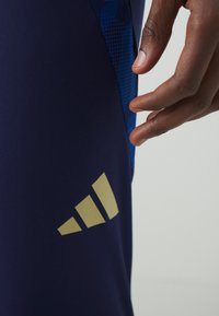Leggings de sport navy en tissu extensible avec un panneau latéral à motifs bleus et un logo Adidas doré en bas à l'avant.