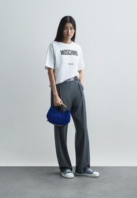 Λευκό κοντομάνικο μπλουζάκι με στάμπα "MOSCHINO Milano", γκρι ψηλόμεσο παντελόνι, μπλε τσάντα χειρός και ανοιχτά μπλε αθλητικά παπούτσια. Λείες υφές.