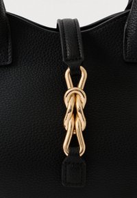 Detailný záber na čiernu koženú kabelku s textúrou, s prepleteným zlatým kovovým reťazcom, ktorý spája dva kožené popruhy.