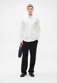 Λευκό πουκάμισο με κουμπιά, μαύρο παντελόνι, κρατώντας μαύρη τσάντα. Κλασική εφαρμογή, δομημένος σχεδιασμός, ομαλή υφή, μινιμαλιστικό στυλ.