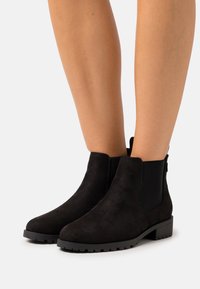 Stivali alla caviglia neri in suede con pannelli laterali elastici e suole in gomma testurizzata. Presentano una punta arrotondata e un tacco basso a blocco.